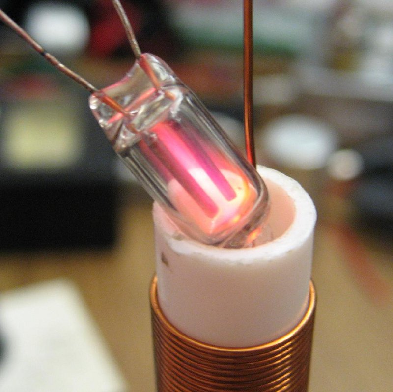 Purplish glow from NE-2 bulb in electric field of Tesla coil secondary.